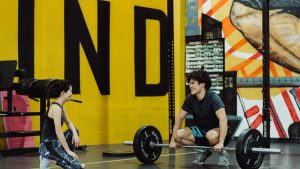 Two young adults in a gym participating in a weightlifting session, sharing a positive moment.